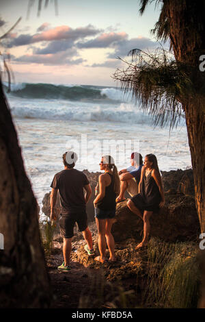 Hawaii, Oahu, North Shore, astanti guardare un grande rigonfiamento in rotolo al tramonto a pupukea beach park sulla sponda nord Foto Stock