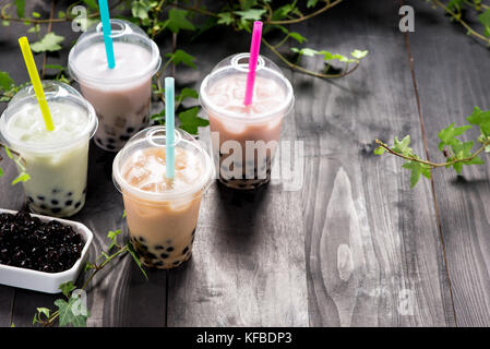 Varietà di tè di bolla in bicchieri di plastica con cannucce su un tavolo di legno. Foto Stock