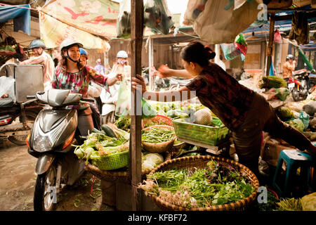 Il Vietnam, Hanoi, una donna e suo figlio sul loro ciclomotore acquistare ortaggi in chau mercato lungo Foto Stock