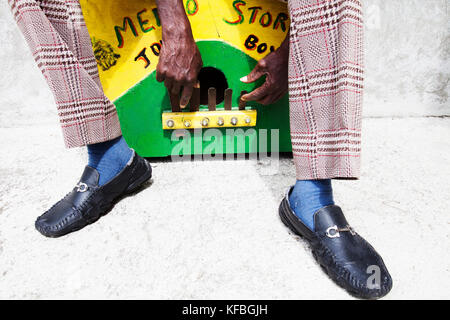 Giamaica, Port Antonio. Derrick "Johnny' Henry del Mento Band, il Jolly Boys, seduto e giocare la casella marumba. Foto Stock