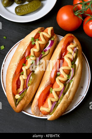 Gustosi piatti caldi i cani con pomodoro, marinato cetrioli, cipolla su sfondo scuro. vista superiore Foto Stock