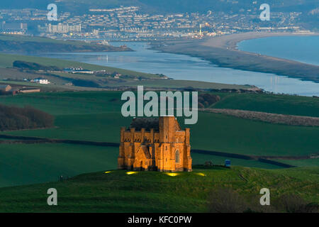 Abbotsbury, Dorset, Regno Unito. Il 27 ottobre 2017. Regno Unito Meteo. Santa Caterina la cappella a Abbotsbury nel Dorset è illuminato al tramonto per l annuale luminarie incantata evento a Abbotsbury giardini subtropicali in una serata di cielo sereno e venti leggeri con una vista lungo la flotta verso l'isola di Portland. Il giorno finale di luminarie presso i giardini è domenica 29 ottobre. Photo credit: Graham Hunt/Alamy Live News Foto Stock