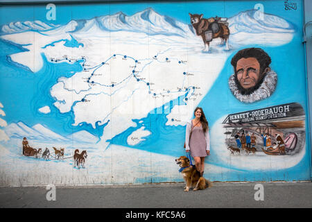 Stati Uniti d'America, Alaska, Anchorage, locale lauren pone con il suo cane di fronte all'Iditarod murale nel centro cittadino di Anchorage Foto Stock