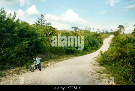 BELIZE, Punta Gorda, Toledo, un ragazzo accompagna la sua bici giù per la strada nei pressi delle rovine di Lubantuun Foto Stock
