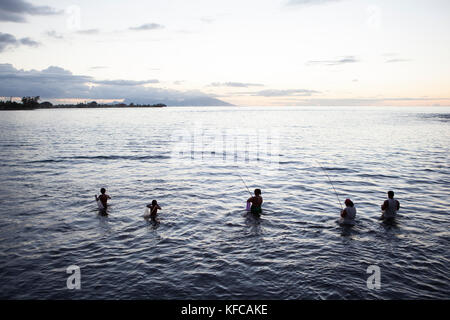 Polinesia francese, Tahiti. Spiaggia di sabbia nera di Tahiti. La gente del posto la pesca in acqua al tramonto. Foto Stock