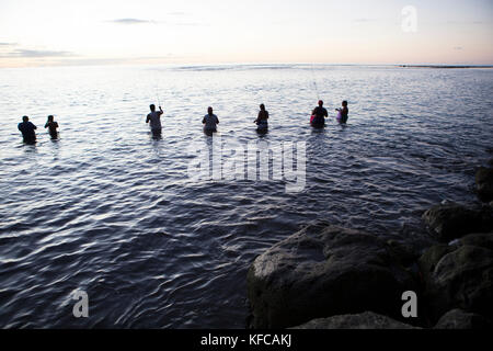 Polinesia francese, Tahiti. Spiaggia di sabbia nera di Tahiti. La gente del posto la pesca in acqua al tramonto. Foto Stock