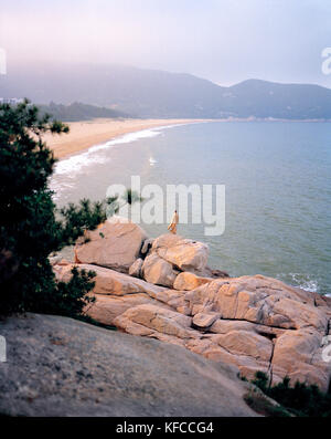 Cina, putou shan, una vista in elevazione del monaco in piedi su una roccia di fronte a migliaia di passi beach Foto Stock