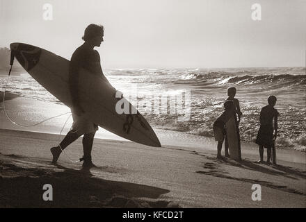 Stati Uniti d'America, Hawaii, Oahu, surfer cammina giù per il surf in spiaggia al tramonto, la North Shore (b&W) Foto Stock