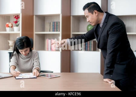 Segretario asiatica sottolinea quando il suo manager è il puntamento e viene imputato per un lavoro difettoso. Segretario e manager in ufficio. Foto Stock