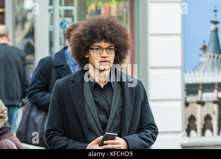 Giovane con un'acconciatura afro a camminare in una città di Brighton, East Sussex, Inghilterra, Regno Unito. Foto Stock