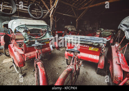 Risciò ciclo e le parti di ricambio per lettiera un rickshaw garage o workshop in Indonesia. Sudest Asiatica di modalità di trasporto. I demolitori per cantiere usato rickshaws Foto Stock