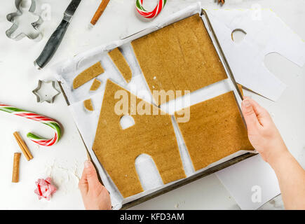 Preparazione per il natale, una persona, le mani nel telaio, fa una casa di panpepato. La ragazza è in possesso di una teglia da forno con la pasta in forma di casa de Foto Stock