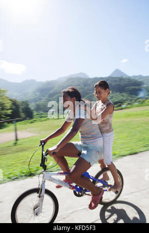 Polinesia Francese, Moorea. Bambini locali lo skateboard e mountain bike. Foto Stock