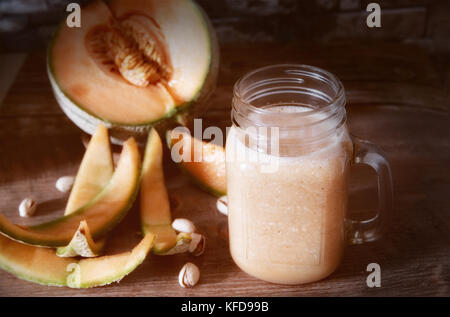 Gustosi frullati di melone-melone in un vasetto di vetro, intero e mature a fette di melone organico-melone su sfondo di legno rustico e accogliente atmosfera. Foto Stock