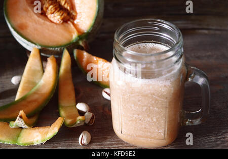 Gustosi frullati di melone-melone in un vasetto di vetro, intero e mature a fette di melone organico-melone su sfondo di legno rustico e accogliente atmosfera. Foto Stock