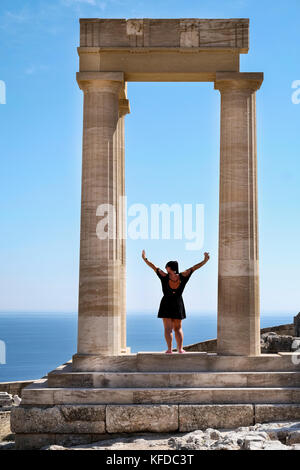 Una donna pone per un'immagine tra le colonne di Lo stoa ellenistico all'interno dell'Acropoli di Lindos sulla isola greca di Rodi Foto Stock