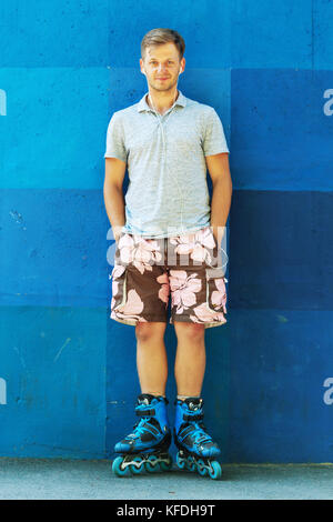 Ritratto di felice bel giovane rullo in pattini inline in piedi contro la parete di blu. Foto Stock