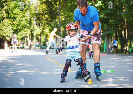 Ritratto di simpatici baby boy con inline skating istruttore nel parco learining a pattinare. Foto Stock