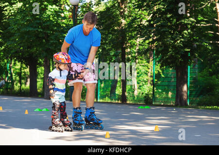 Ritratto di simpatici baby boy con inline skating istruttore nel parco learining a pattinare. Foto Stock