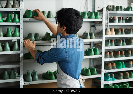 Lavoratori autonomi cobbler in piedi di fronte a ripiani con forme di calzature e scegliendo il modello di scarpe per il nuovo ordine Foto Stock