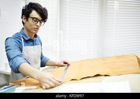 Giovane artigiano prendendo le misure del pezzo di tessuto dai luoghi di lavoro prima del taglio Foto Stock