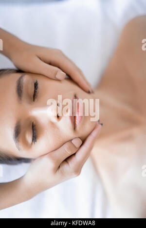Rilassata giovane donna avente la sua faccia massaggiato in dayspa salon Foto Stock