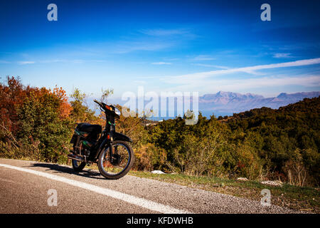 Lo scooter, moto sulla strada che scende dal monte più alto (Pantocratore) sull'isola del Mar Ionio Corfù, Grecia. Rocce, bellissimi colori autunnali Foto Stock