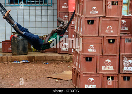 Il Burkina Faso, Provincia Poni, Gaoua, beer pub, Brakina cassette di birra, uomo in amaca Foto Stock