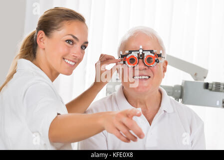 Sorridente giovane femmina all'ottico optometrista controllo maschio senior paziente la visione con telaio di prova Foto Stock