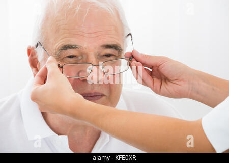 Close-up di un ottico aiutando senior paziente di sesso maschile con nuovi occhiali Foto Stock