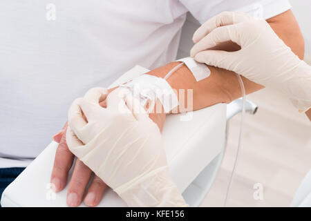 Close-up del medico la mano con flebo IV inserito in mano del paziente Foto Stock