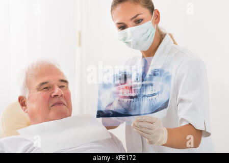 Giovani donne medico mostra apparecchiature odontoiatriche a raggi X per Senior paziente di sesso maschile in clinica Foto Stock