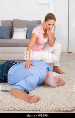 Scioccato giovane donna Guardando Lei svenuta disabilitato padre giacente su un tappeto Foto Stock