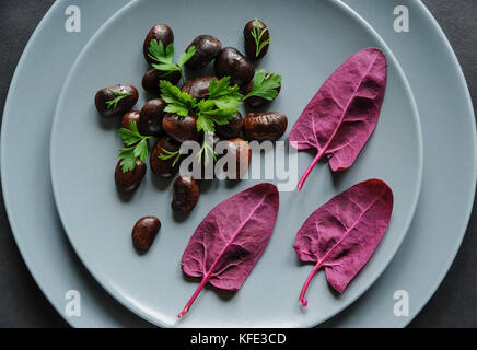 Piastra con fagioli scuro e rosso foglie di spinaci su uno sfondo scuro. Foto Stock