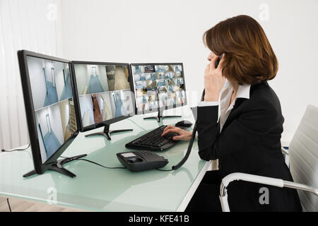 Operatore femmina guardando a più riprese sui computer mentre si parla al telefono Foto Stock