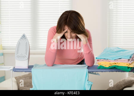 Giovane donna esaurito durante la stiratura di panni a casa Foto Stock