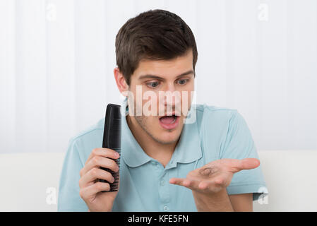 Giovane Azienda pettine guardando i capelli di perdita Foto Stock