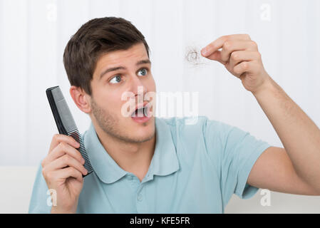 Giovane Azienda pettine guardando i capelli di perdita Foto Stock