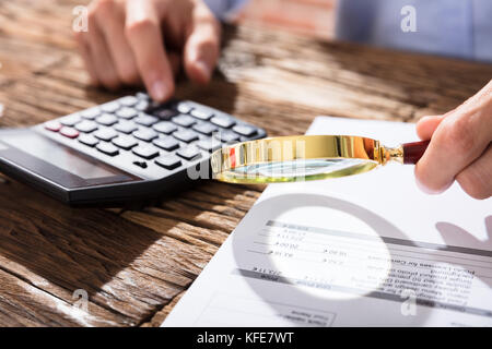 Close-up di ragioniere con lente di ingrandimento e calcolatrice mentre il calcolo di finanza Foto Stock