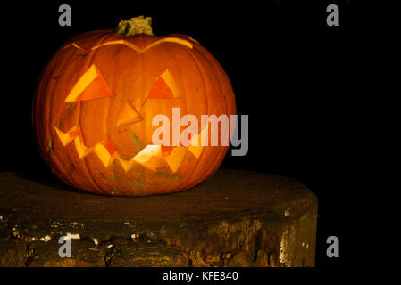 Spooky Zucca di Halloween con tagliare volto illuminato con una candela su un ceppo di albero in legno scuro. Foto Stock