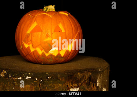 Spooky Zucca di Halloween con tagliare volto illuminato con una candela su un ceppo di albero in legno scuro. Foto Stock