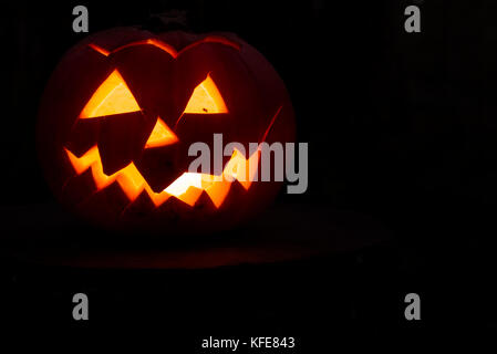 Spooky Zucca di Halloween con tagliare volto illuminato con una candela su un ceppo di albero in legno scuro. Foto Stock