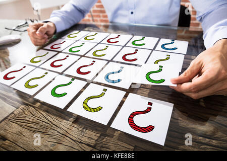 Imprenditore con colorati punto interrogativo sulle note di adesivo sopra la scrivania in ufficio Foto Stock