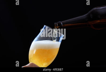 Versare la birra in un bicchiere closeup su uno sfondo nero. Foto Stock