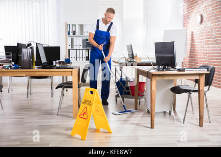 Bidello maschio piano di pulizia con segnale di avvertimento pavimento bagnato in Office Foto Stock