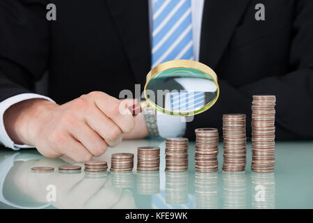 Sezione mediana del giovane imprenditore esaminando monete impilate come grafico a barre nella tabella di office Foto Stock