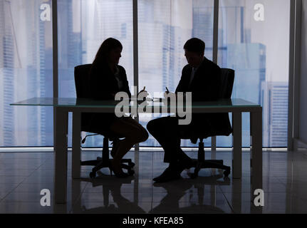 Silhouette dell'imprenditore e imprenditrice discutendo alla scrivania in ufficio Foto Stock