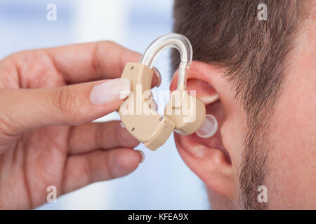 Immagine ritagliata del medico inserimento di protesi in uomo l orecchio Foto Stock