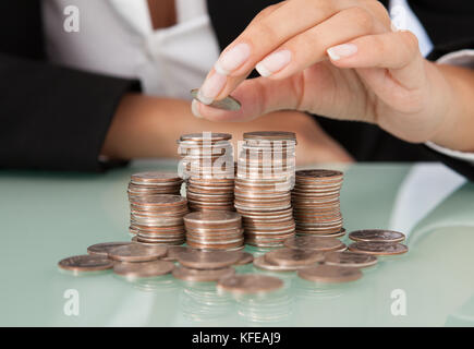 Primo piano della imprenditrice la mano di monete di stacking a scrivania in ufficio Foto Stock