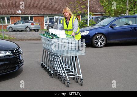 Un dipendente di sesso femminile la raccolta di carrelli della spesa al di fuori di un ramo della catena di supermercati waitrose a Tenterden nel Kent, in Inghilterra il 17 maggio 2012. Foto Stock